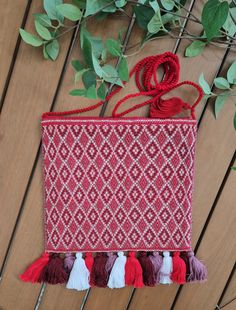 a red and white bag with tassels hanging from it's side on a wooden surface