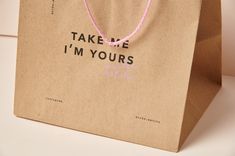 a brown paper bag that says take me i'm yours with pink string on it