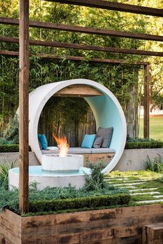 an outdoor fire pit surrounded by greenery and wooden posts, with seating around it