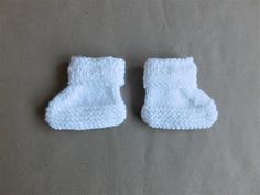 two pairs of white knitted baby booties sitting on top of a gray surface