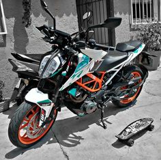 an orange and white motorcycle parked next to a skateboard on the sidewalk in front of a building