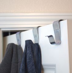 two pairs of clothes hanging from hooks on a white door handle and coat hanger