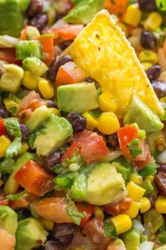 a tortilla chip being held over a salad with black beans, corn and avocado