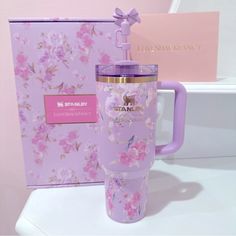 a pink and purple travel mug next to a gift box on a white countertop