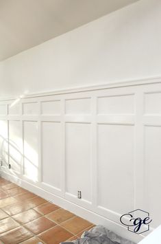 an empty room with tile flooring and white paneling on the walls, in front of a window