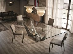 a glass dining table surrounded by chairs in a living room with wooden floors and windows