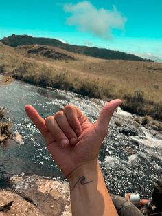 a person is holding their hand up in the air near a river with mountains in the background