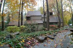 a house in the woods with lots of leaves on the ground and trees around it