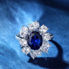 a blue and white diamond ring sitting on top of a blue cloth with diamonds around it