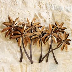 three metal palm trees mounted to the side of a stone wall in front of a white stucco wall