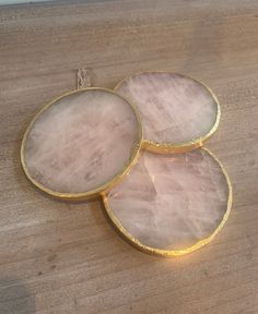 three slices of pink agate on a wooden surface with gold trim around the edges