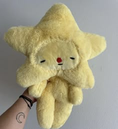 a hand holding a yellow teddy bear with its eyes closed and one eye partially closed