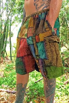 a man with tattoos standing in the woods wearing shorts that have different colors and designs on them