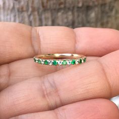 a hand holding a gold ring with emeralds and white diamonds on the inside of it