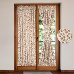 an open window with floral curtains next to a plate on the floor in front of it