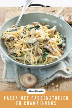 a bowl filled with pasta and mushrooms on top of a wooden cutting board next to garlic