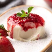 two strawberries sit on a plate next to a small bowl of yogurt