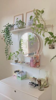 a white dresser topped with lots of potted plants next to a round mirror on the wall