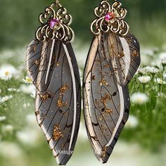 two brown and white butterfly wings with pink stones on them are hanging from gold filigrees