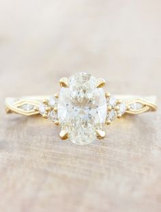 an oval cut diamond ring with three small diamonds on the band and side stones in yellow gold