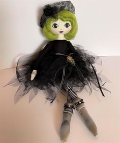 a doll with green hair wearing a black dress and gray shoes sitting on top of a table