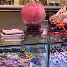 an assortment of jewelry on display in a store window with pink glass vases and other items