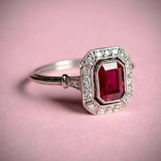 a close up of a ring with a red stone in it on a pink surface