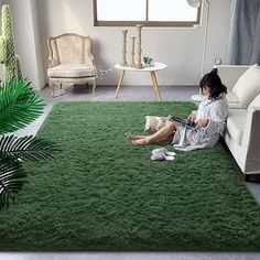 a woman sitting on a green rug in a living room next to a white couch