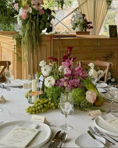 the table is set with white and pink flowers, green grapes, and greenery