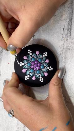 a woman is painting a flower on a black rock with blue and pink flowers painted on it