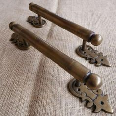 two antique brass door handles and knobs on a beige fabric background, one with an ornate design