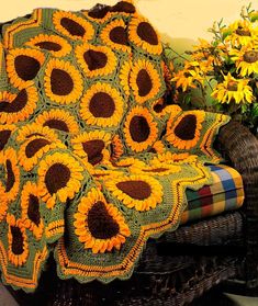 a couch with a crocheted blanket on top of it and sunflowers in the background