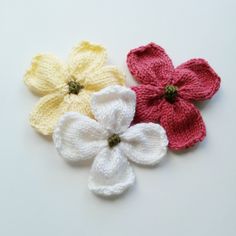 three crocheted flowers sitting on top of a white table next to each other