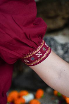 a woman's arm wearing a red dress and bracelet with flowers in the background