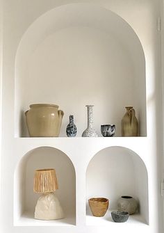 three shelves with vases and other items on them in a white walled room,