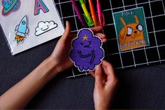 a person holding a sticker next to some pens and magnets on a table