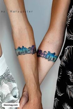 two people are holding hands with tattoos on their arms and one is showing the city