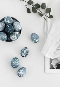 blue and white painted eggs in a bowl next to a plant on a white surface