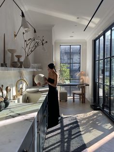 a woman in a black dress standing at a kitchen counter next to an open window