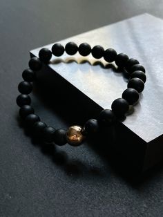 This sleek matte black bracelet is made from genuine AAA+ tourmaline stones featuring a single 14K gold filled bead to balance the bracelet. This beaded stretch bracelet can be worn by both men and women, the perfect gift for him or her. Tourmaline is a natural gemstone that is well known as being a protection stone. It is also associated with grounding, positivity and health. It is thought that wearing this stone helps to dispel negative thoughts and calm the mind in order to bring positive energy into your body.  The bracelet stretches and is made to be one size fits all. It is also hypoallergenic, lead and nickel free which is great for those who have sensitive skin. Size: one size fits all Bead Size: 8 mm Material: 14K gold filled & tourmaline Minimalist Black Bracelet For Meditation, Minimalist Black Bracelets For Meditation, Minimalist Black Beaded Bracelets For Meditation, Mens Stretch Bracelets, Black Tourmaline Bracelet, Tourmaline Bracelet, Black Bracelet, Crystal Healing Stones, Yoga Bracelet