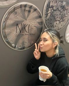 a woman sitting at a table with a cup of coffee in front of her and two clocks on the wall behind her