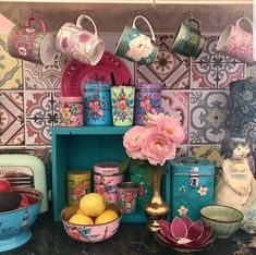 there are many cups and bowls on the shelf in the kitchen with flowers, teapots, and other items