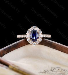 an oval shaped blue sapphire and diamond halo ring on top of a wooden box with writing utensils