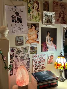 a desk with many pictures on the wall and a lamp in front of it,