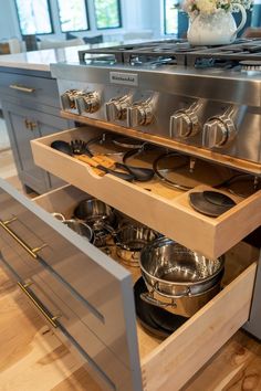 an open drawer in a kitchen with pots and pans on the counter top,