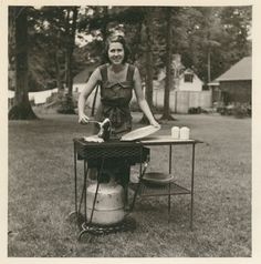 an old photo of a woman ironing clothes on a table in the yard,