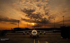 an airplane is sitting on the tarmac at sunset with clouds in the sky behind it