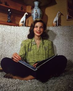 a woman is sitting on the floor with a book in her hands and some figurines behind her