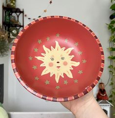 a hand holding a red bowl with a yellow sun painted on the side and stars around it