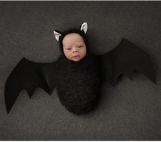 a baby wearing a bat costume laying on top of a gray floor with his eyes closed